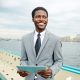 Handsome African American manager looking away with toothy smile while standing on upper deck of ship and checking business emails with help of digital tablet, waist-up portrait shot