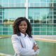 Cheerful smiling female professional posing near office building. Young black woman wearing formal suit, standing with arms crossed and smiling at camera. Career success concept