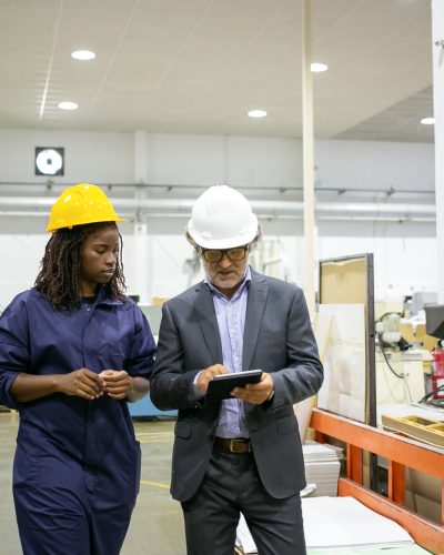 Caucasian manager discussing factory work with African worker. Beautiful pensive young woman working on plant and looking on tablet in supervisor hands. Manufacture and digital technology concept